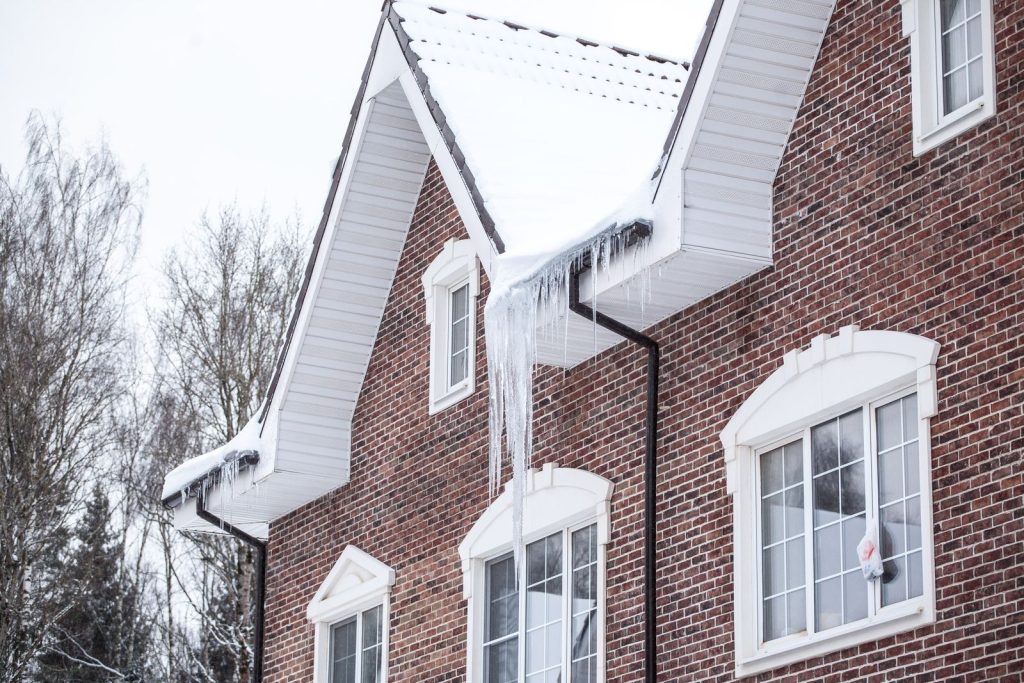 Brick house with snow on the roof and long icicles hanging from the gutters in winter