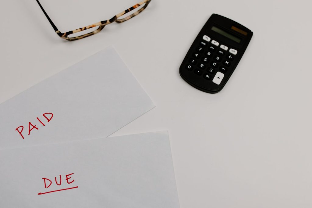 Two envelopes marked paid and due next to a calculator and a pair of glasses on a white desk