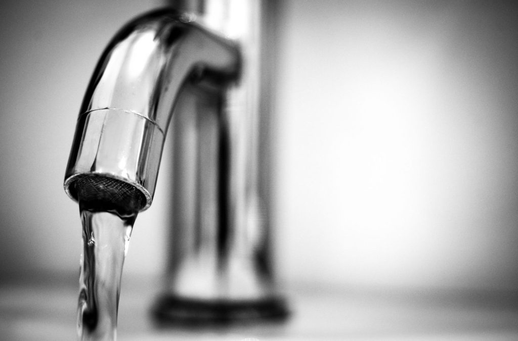 Water running from a stainless steel kitchen faucet, in black and white