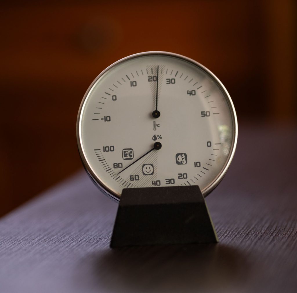 Round analog thermometer and hygrometer on a wooden table showing indoor temperature and humidity