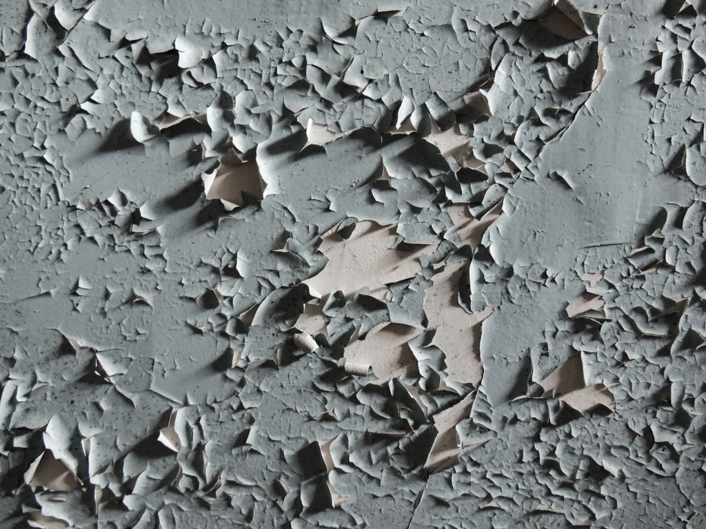 Afbladderende grijze verf op een oude muur, van dichtbij