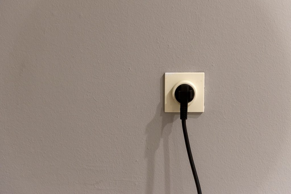 Zwarte stekker in een wit stopcontact op een grijze muur