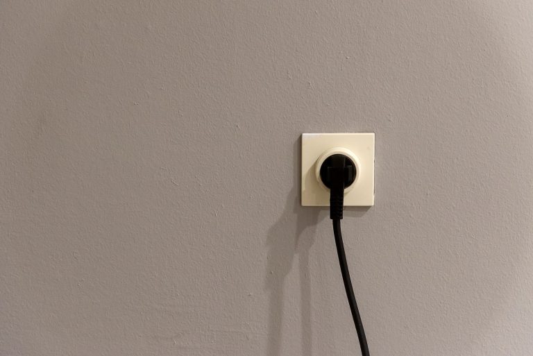 Zwarte stekker in een wit stopcontact op een grijze muur