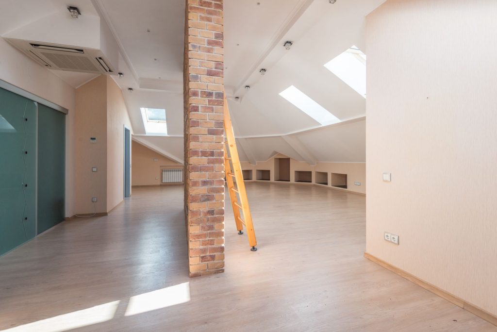 Lichte zolderruimte met dakramen, een bakstenen pilaar en een houten ladder