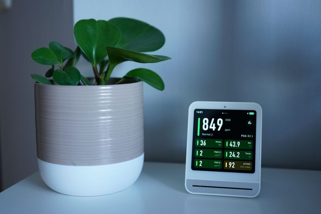 Luchtkwaliteitsmeter met een CO2-waarde van 849 ppm op een bureau naast een plant in een pot