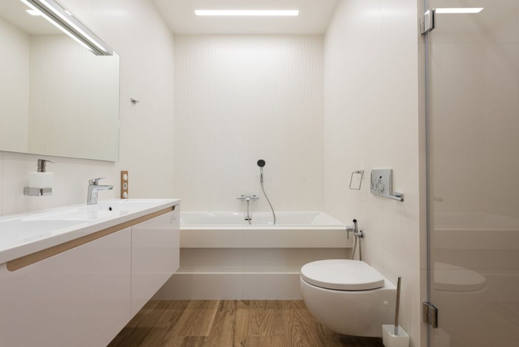 Lichte badkamer met wit plafond, bad, wastafel en inloopdouche met glazen wand