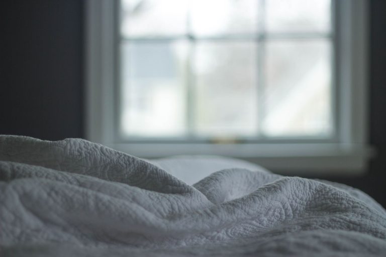 Verfrommeld dekbed op een bed voor een raam met ochtendlicht in een slaapkamer