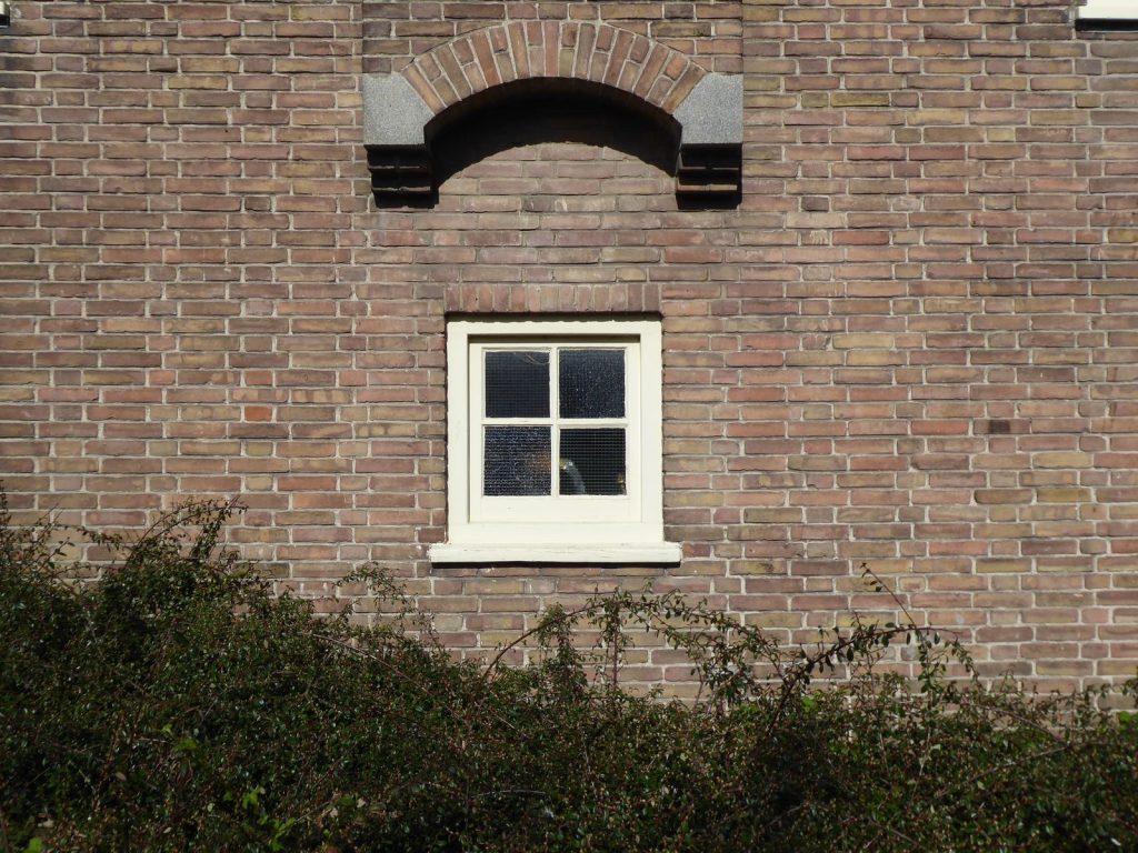 Klein wit raam met kleine ruitjes in een oude bakstenen gevel met een gemetselde boog erboven