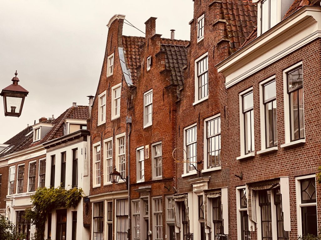 Rij oude bakstenen huizen met trapgevels en een straatlantaarn in een Nederlandse straat