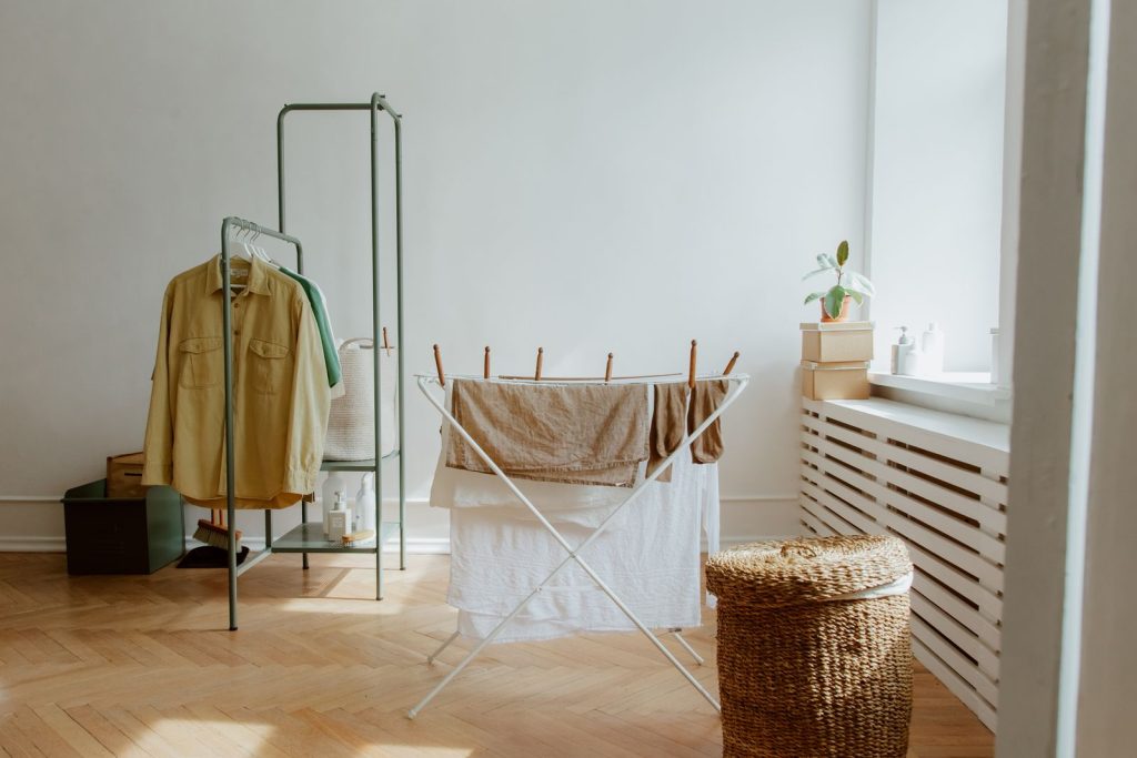 Droogrek met was in een lichte kamer met houten vloer, naast een kledingrek en een radiatorombouw