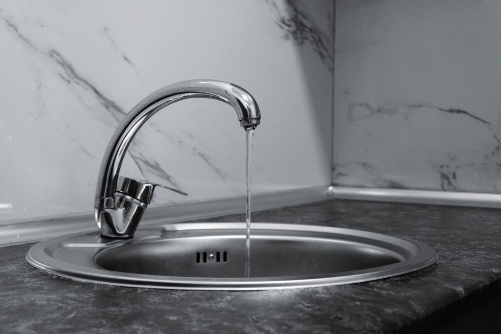Verchroomde keukenkraan met een dunne straal water in een ronde rvs-spoelbak