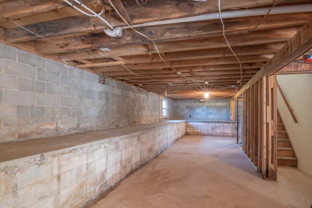 Unfinished basement with concrete block walls, exposed wooden joists and a staircase
