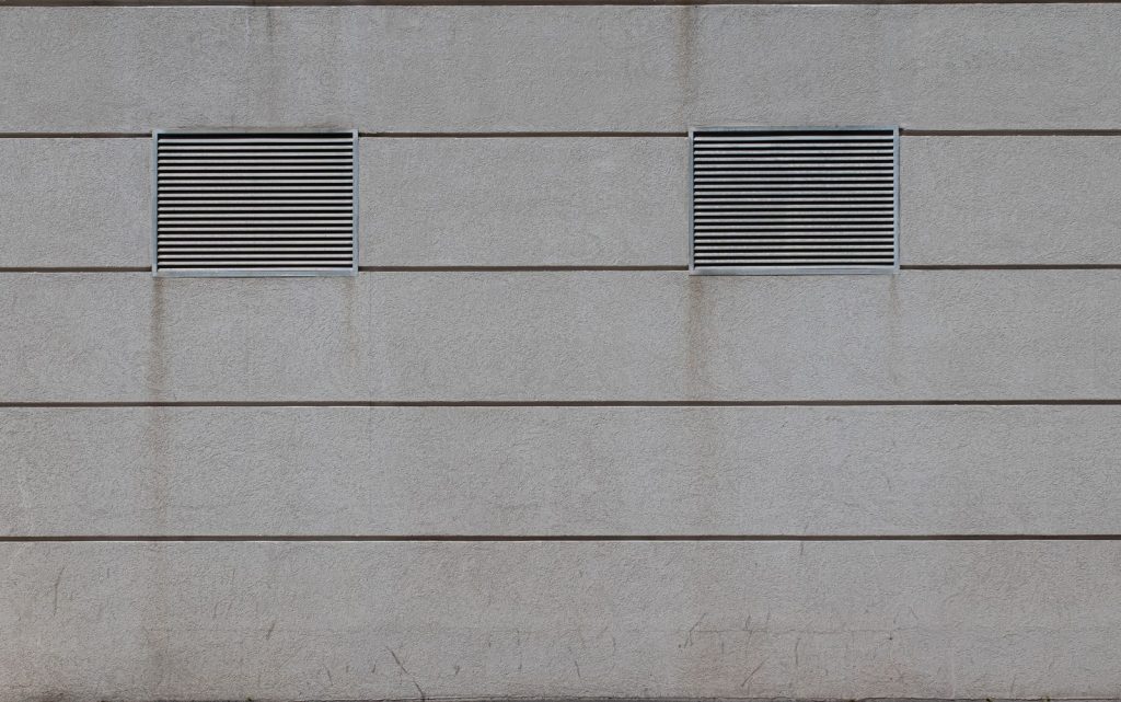 Two rectangular metal ventilation grilles set into a plain gray concrete facade